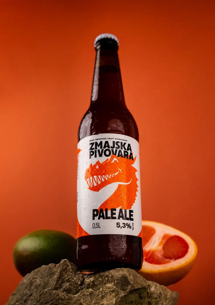 Boca piva Pale Ale na kamenu uz grejp i limetu, na narančastoj pozadini