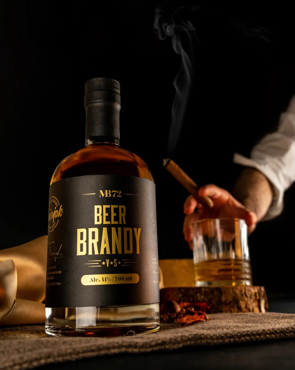 Boca MB72 Beer Brandy uz čašu i ruku s cigarom u tamnom ambijentu