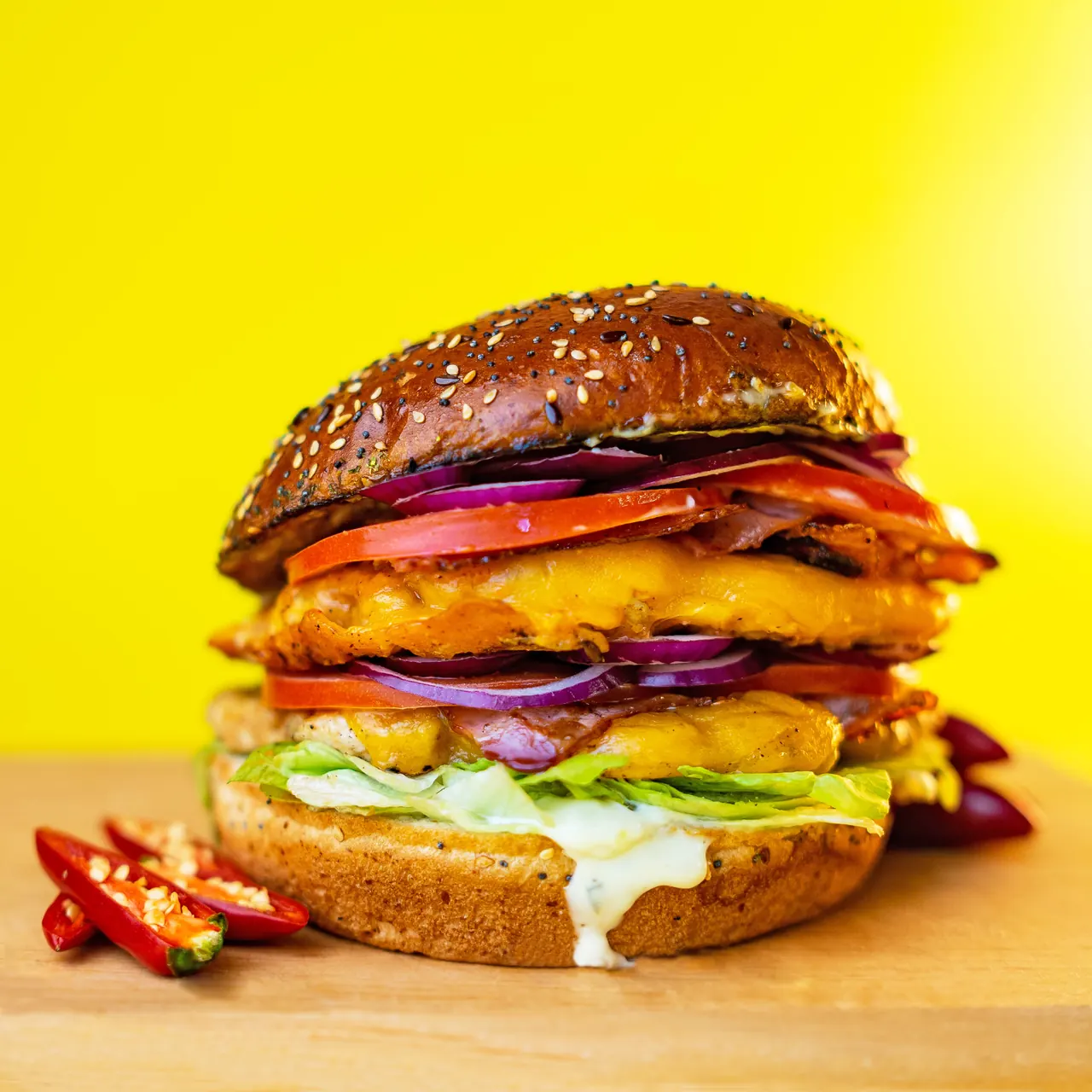 Burger Hot King Chicken s pohanom piletinom, rajčicom, crvenim lukom i čili papričicama na žutoj pozadini